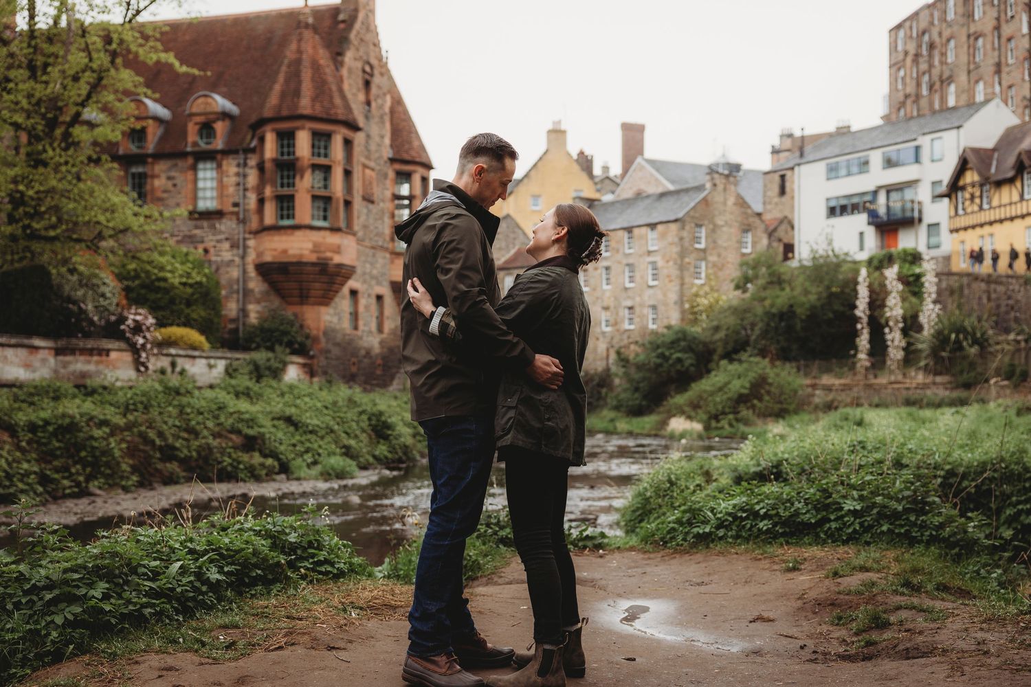 A couple shares a romantic moment in front of historic stone buildings during an engagement photo session.