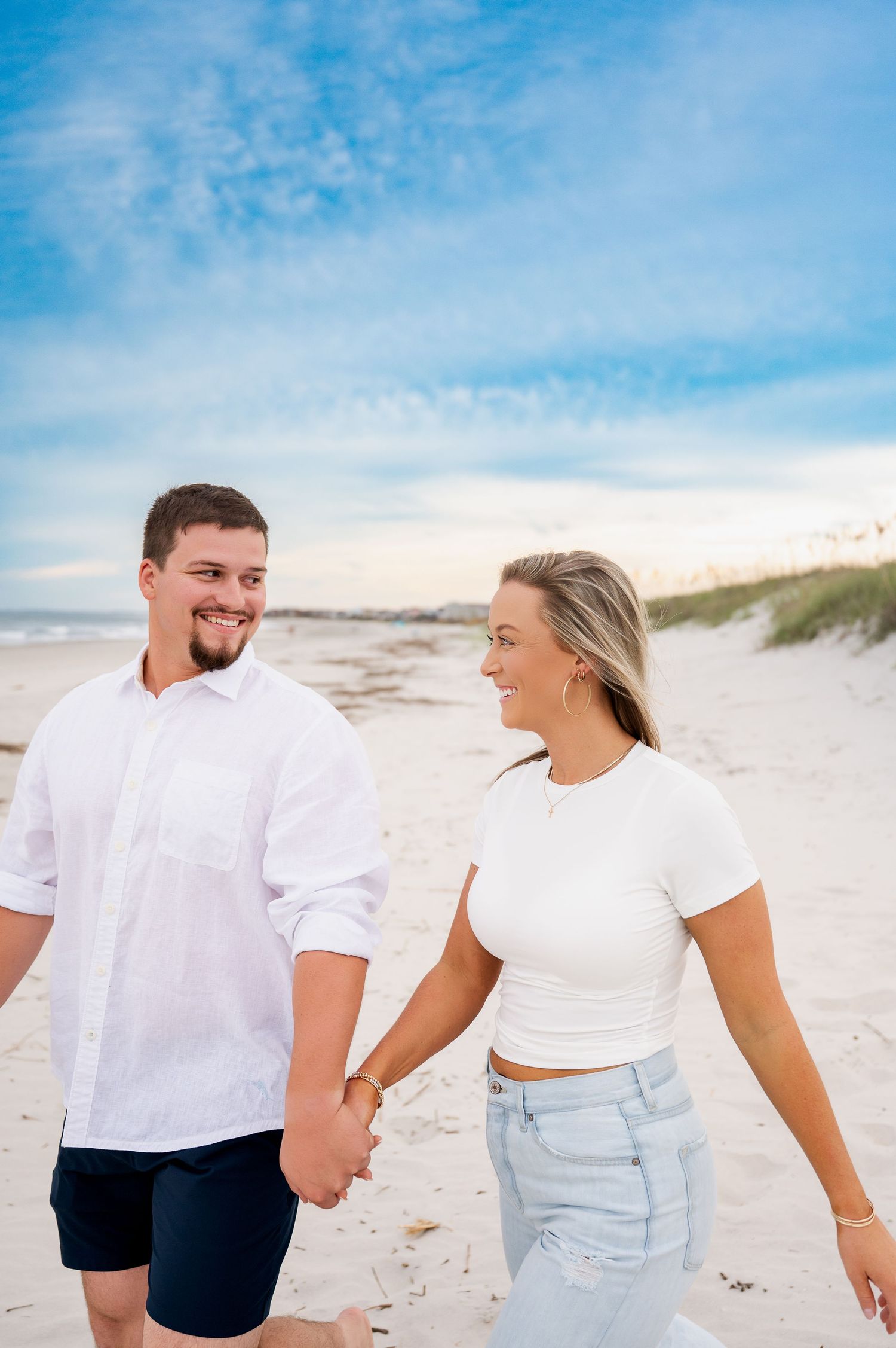 Couple walking hand in hand along pristine beach with white sand and blue skies.