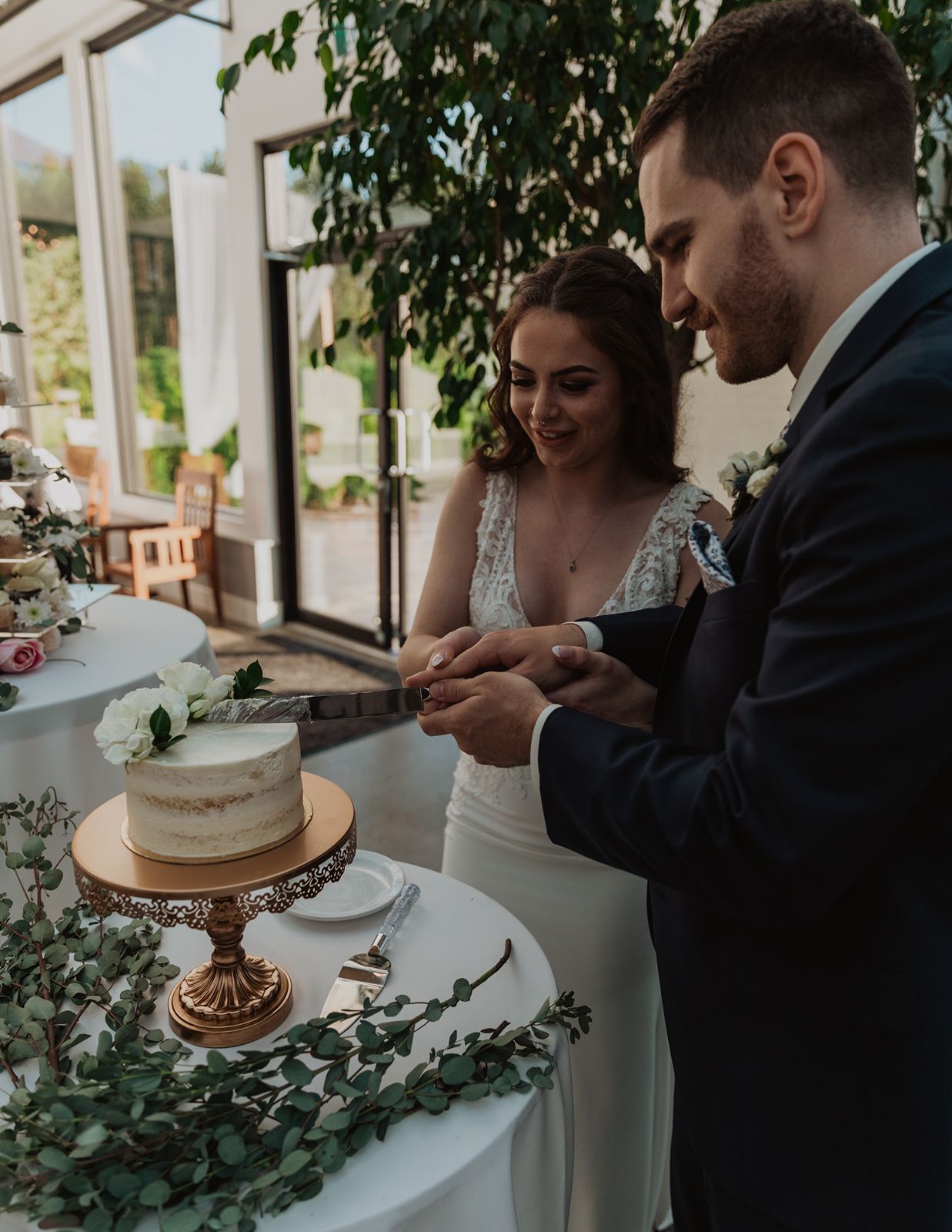 Bride and groom cutting their elegant white wedding cake on a gold stand at their reception.