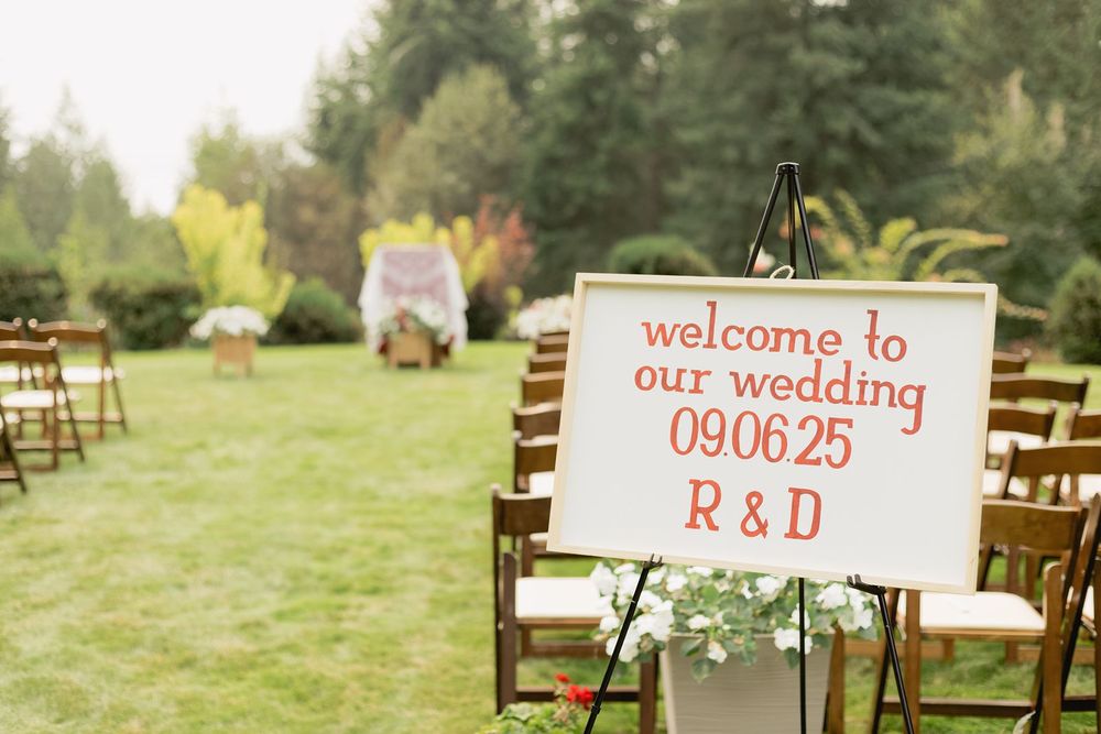 Outdoor wedding welcome sign reading welcome to our wedding 09.06.25 R&D on an easel with wooden chairs.