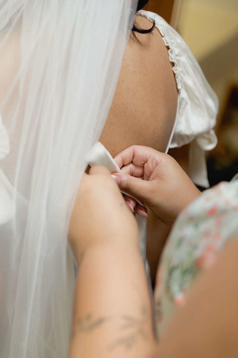 Close-up of hands fastening buttons on back of brides white wedding dress with veil.