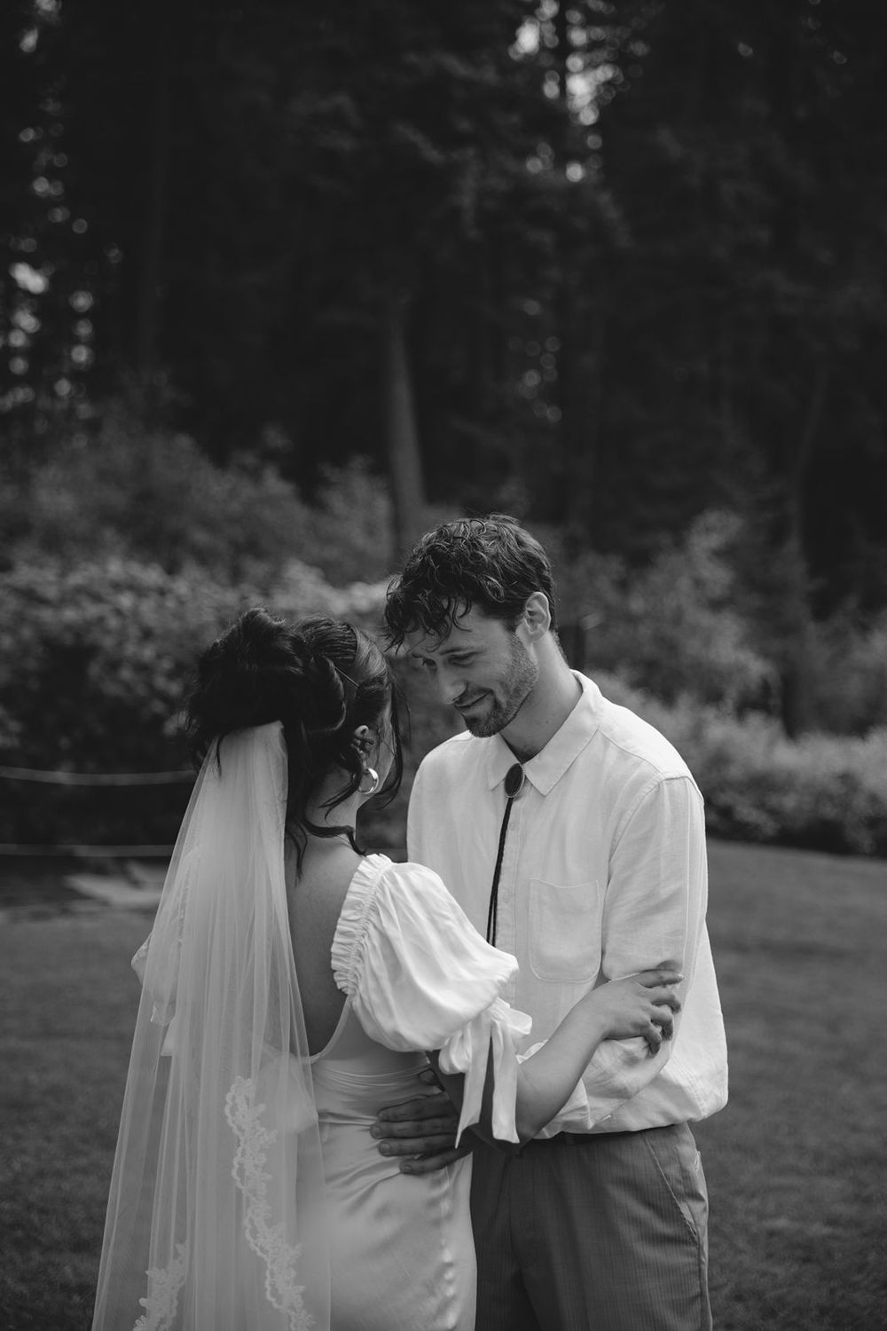 Black and white photo of smiling bride and groom sharing intimate moment in garden setting.