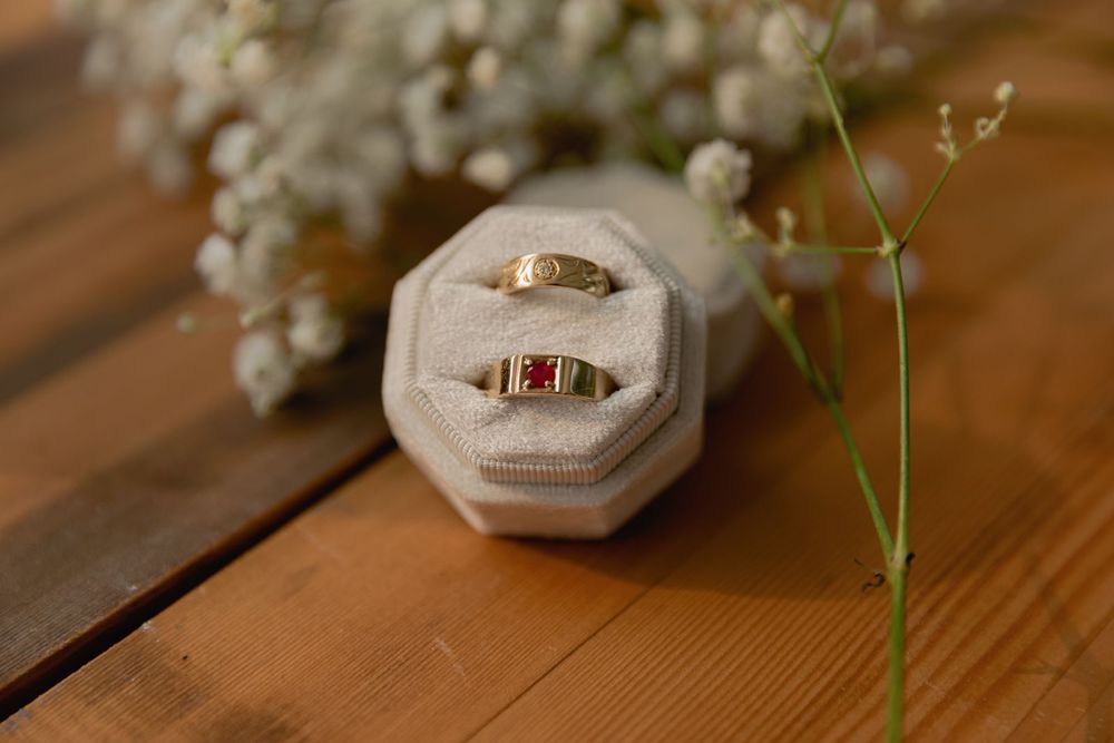 Two gold wedding bands with gemstones displayed in a velvet ring box with white flowers.