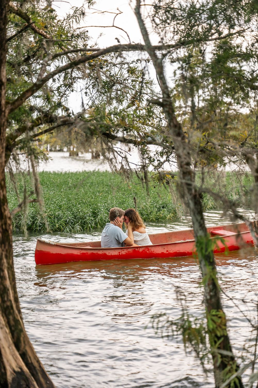 A red canoe drifts along serene waters with overhanging trees creating a natural frame.