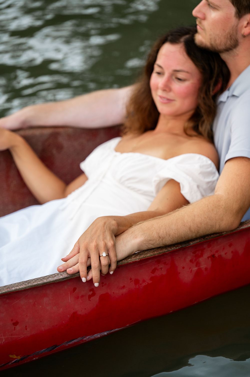 Close-up view of hands resting on the edge of a red canoe during a peaceful water journey.