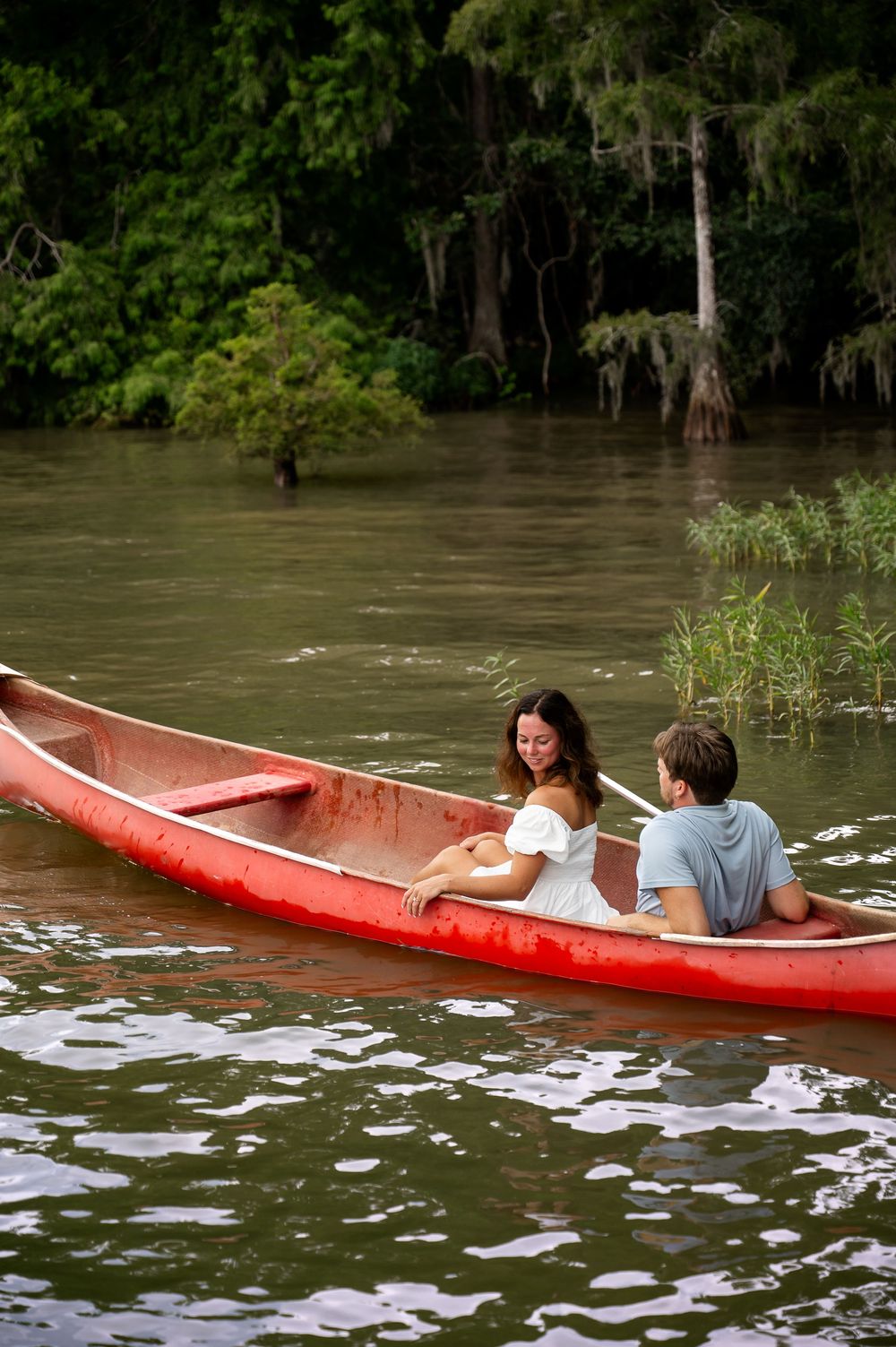 A red canoe floats among lily pads in tranquil waters surrounded by cypress trees.