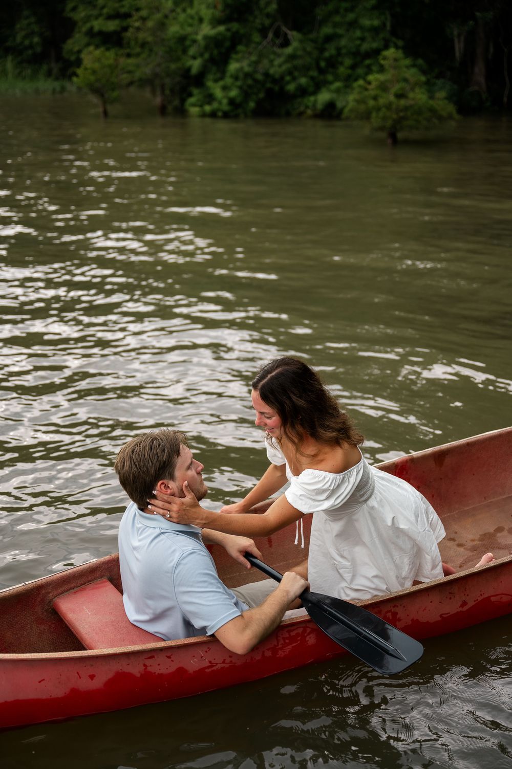 Two people share playful moments while lounging in a red canoe on the water.