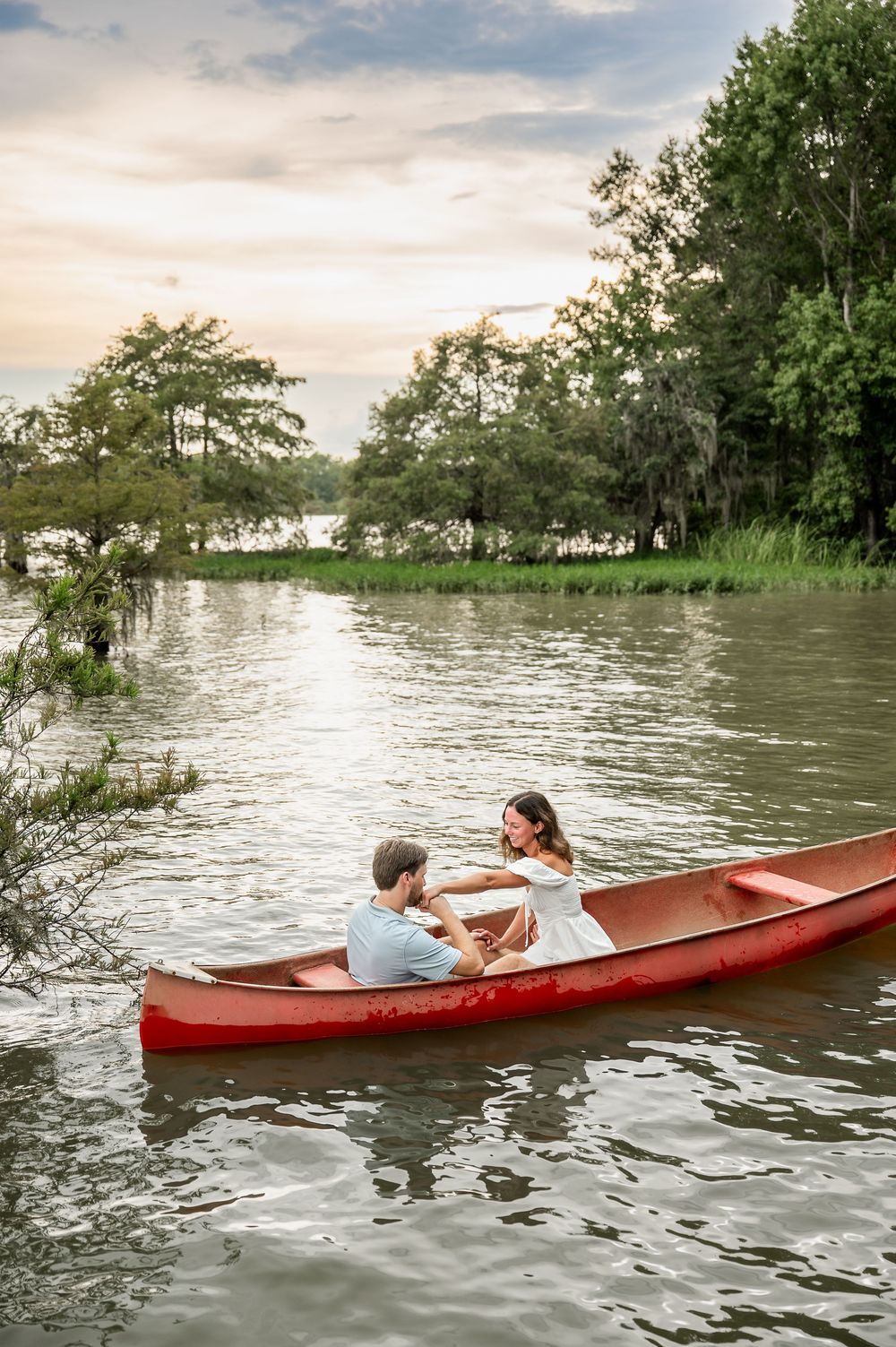 A red canoe drifts on peaceful waters during golden hour with trees lining the shore.