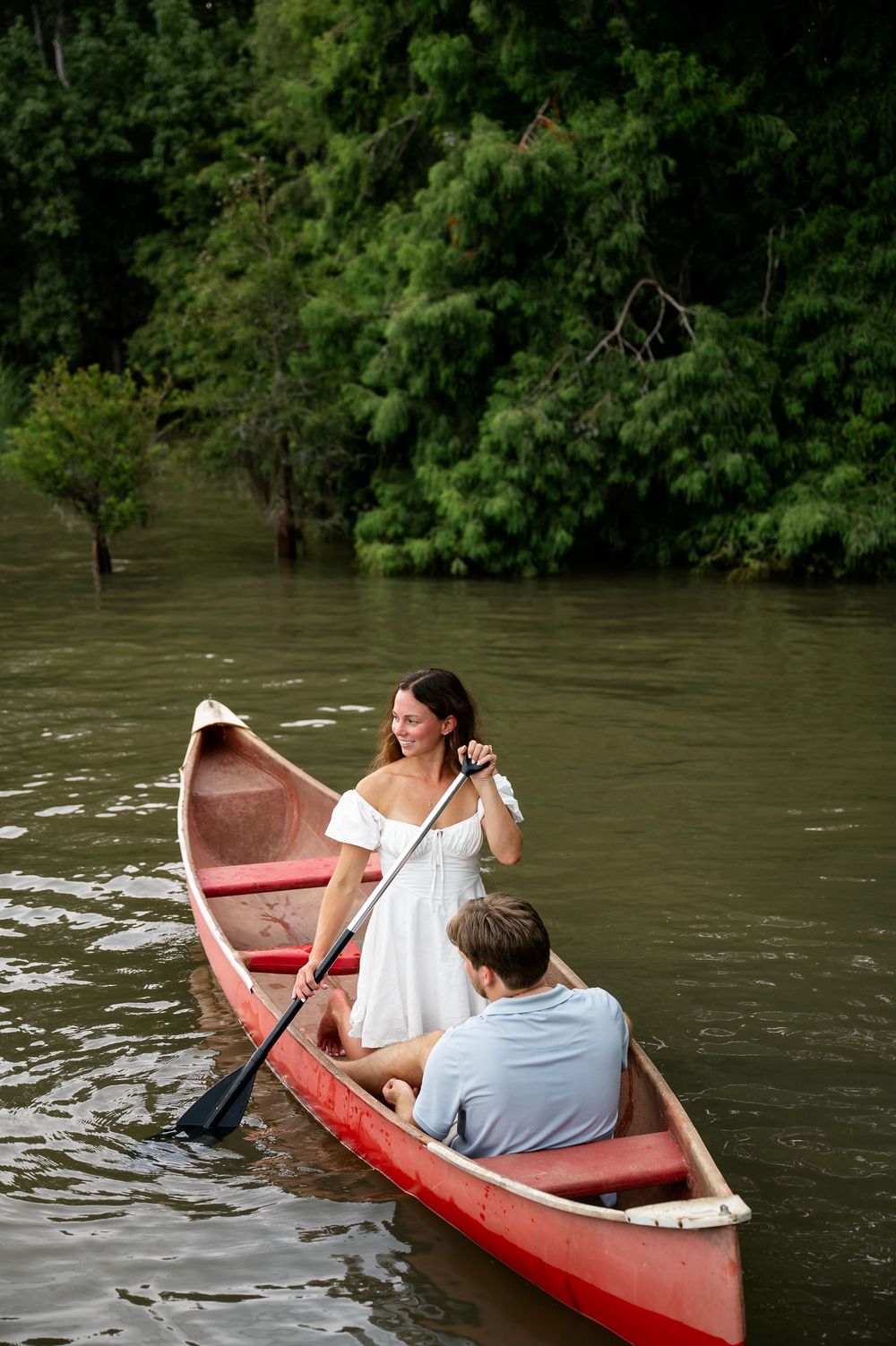 A couple enjoys a romantic canoe ride down a river surrounded by lush green trees.
