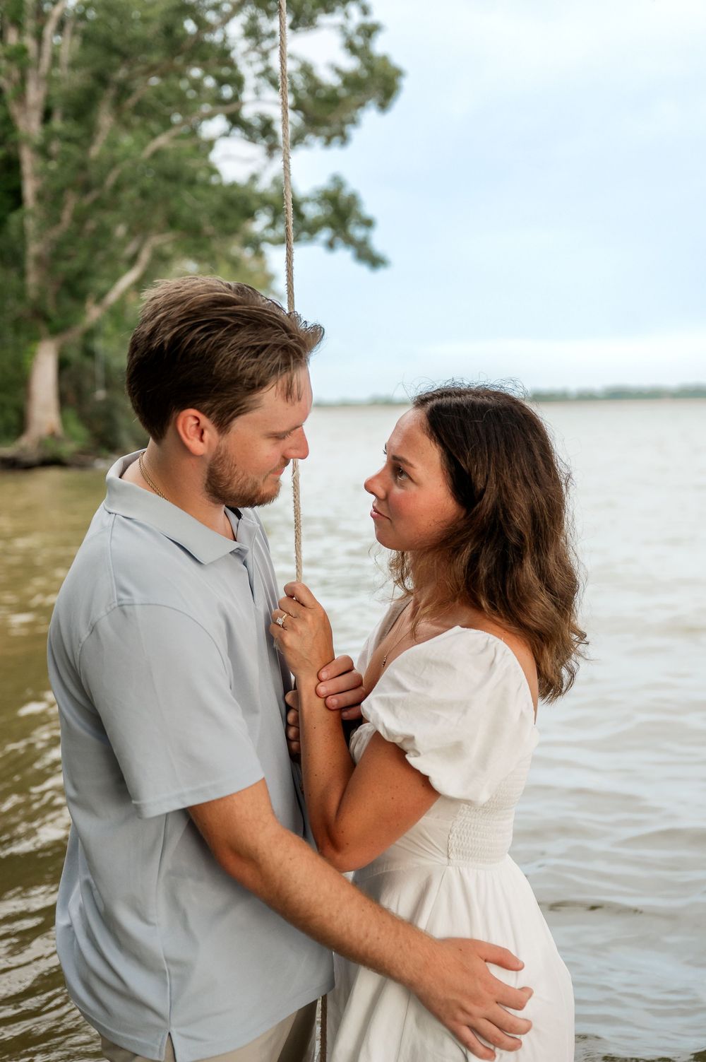 A couple shares an intimate moment while standing in river water during sunset.