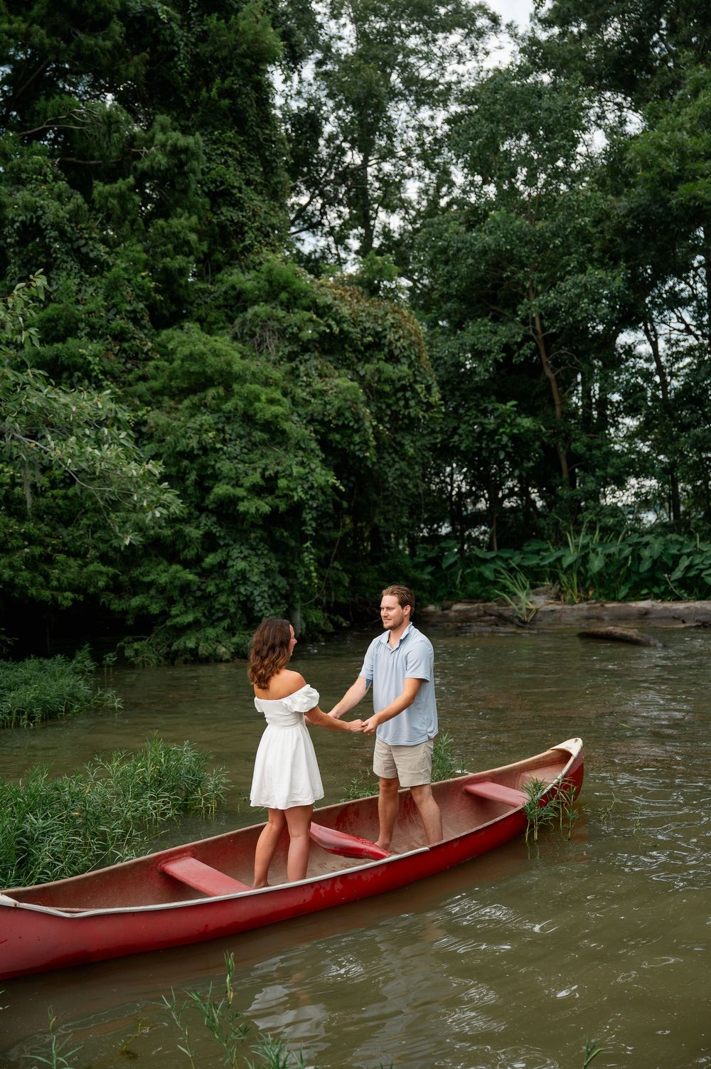 Standing together in a red canoe on a peaceful river surrounded by green trees.