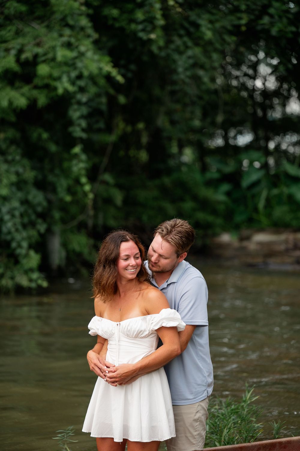Tender moment shared by the riverbank with lush forest backdrop.