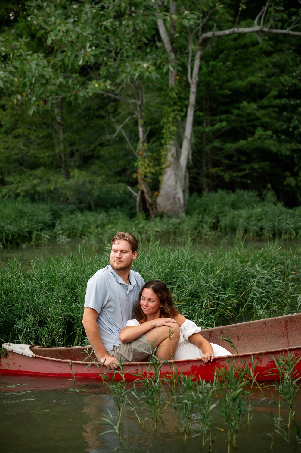 Two people share an intimate moment while lounging in a red canoe amidst marsh grasses.