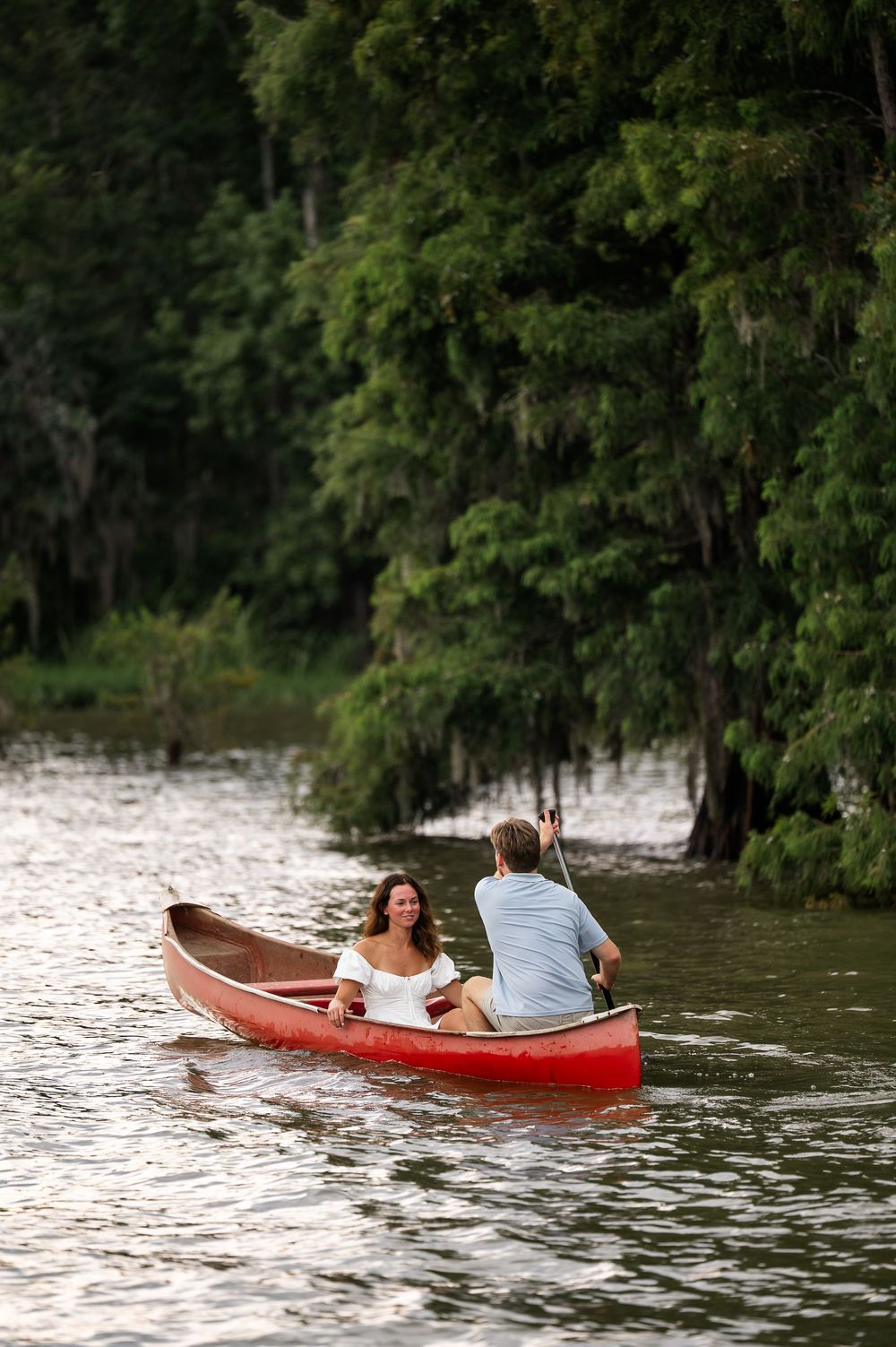 A red canoe floats across rippling water with tree-lined shores in the background.