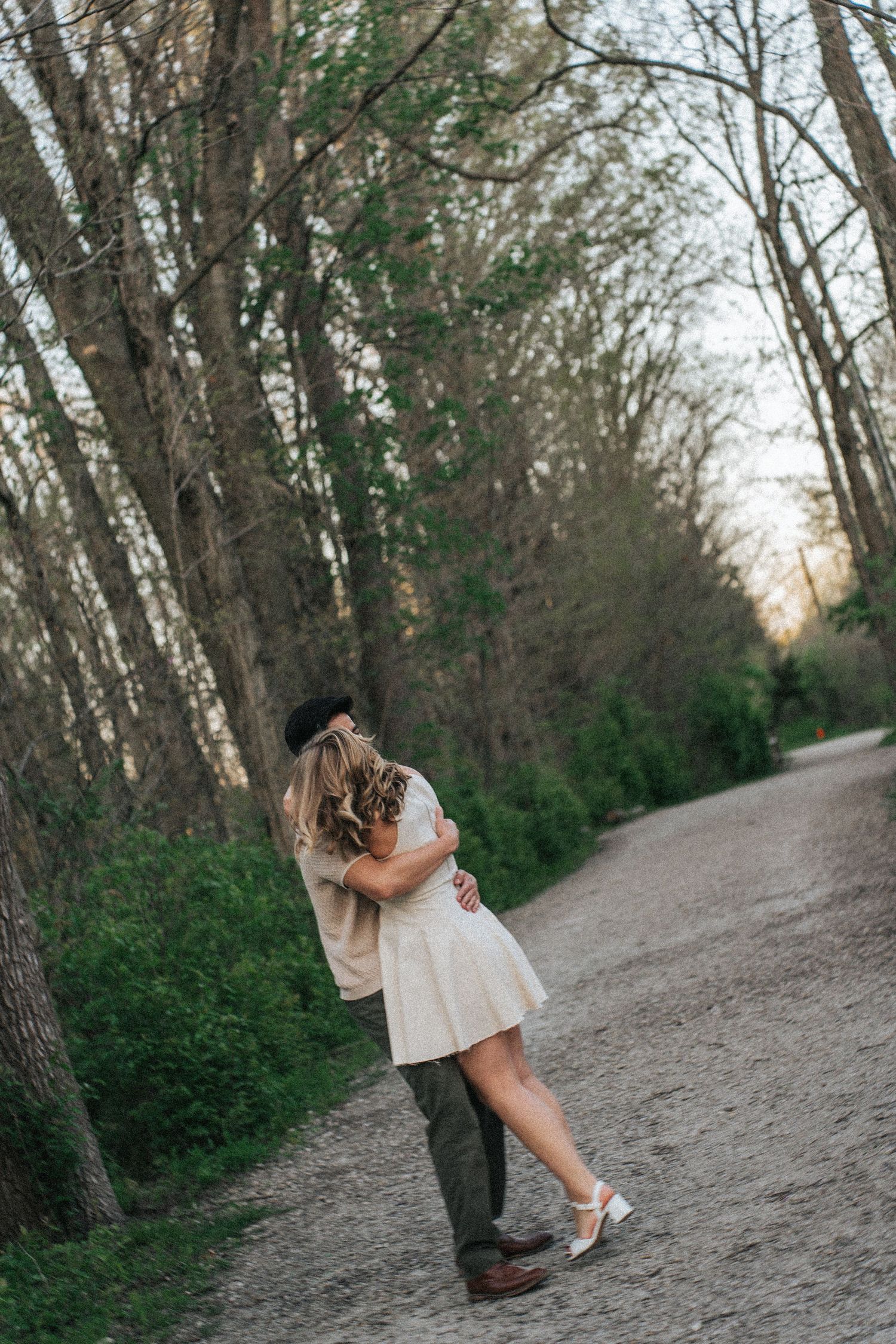 Romantic engagement photos of couple embracing on a wooded trail at sunset.
