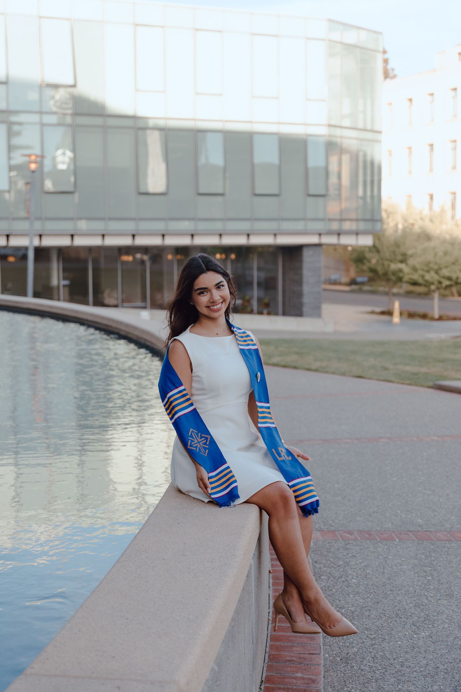 Graduate sits on the edge of a fountain with her sash draped around at the University of San Francisco. By Bay Area Graduation Photographer.