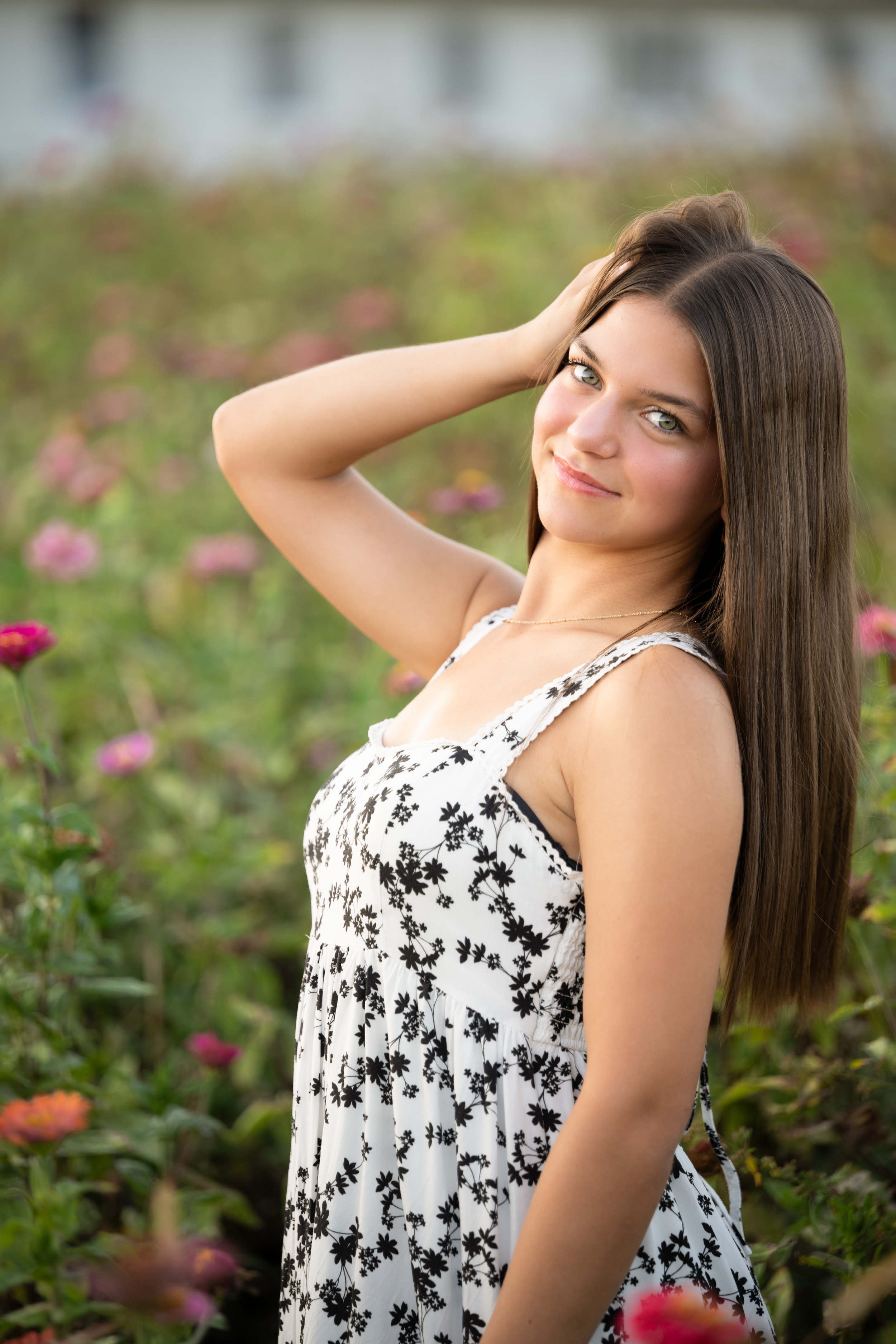 Senior photography rep dressed in a black and white floral dress and poses gracefully with blooming pink flowers in the background.
