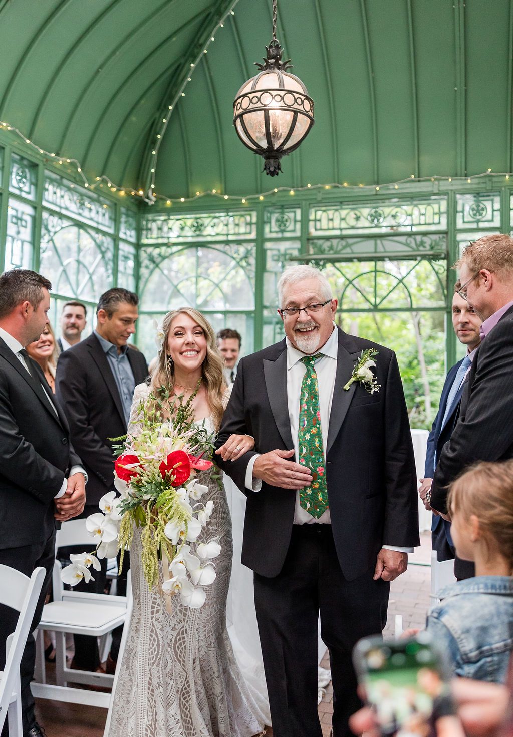 Wedding ceremony taking place in an elegant glass conservatory with ornate Victorian architecture and hanging lantern.