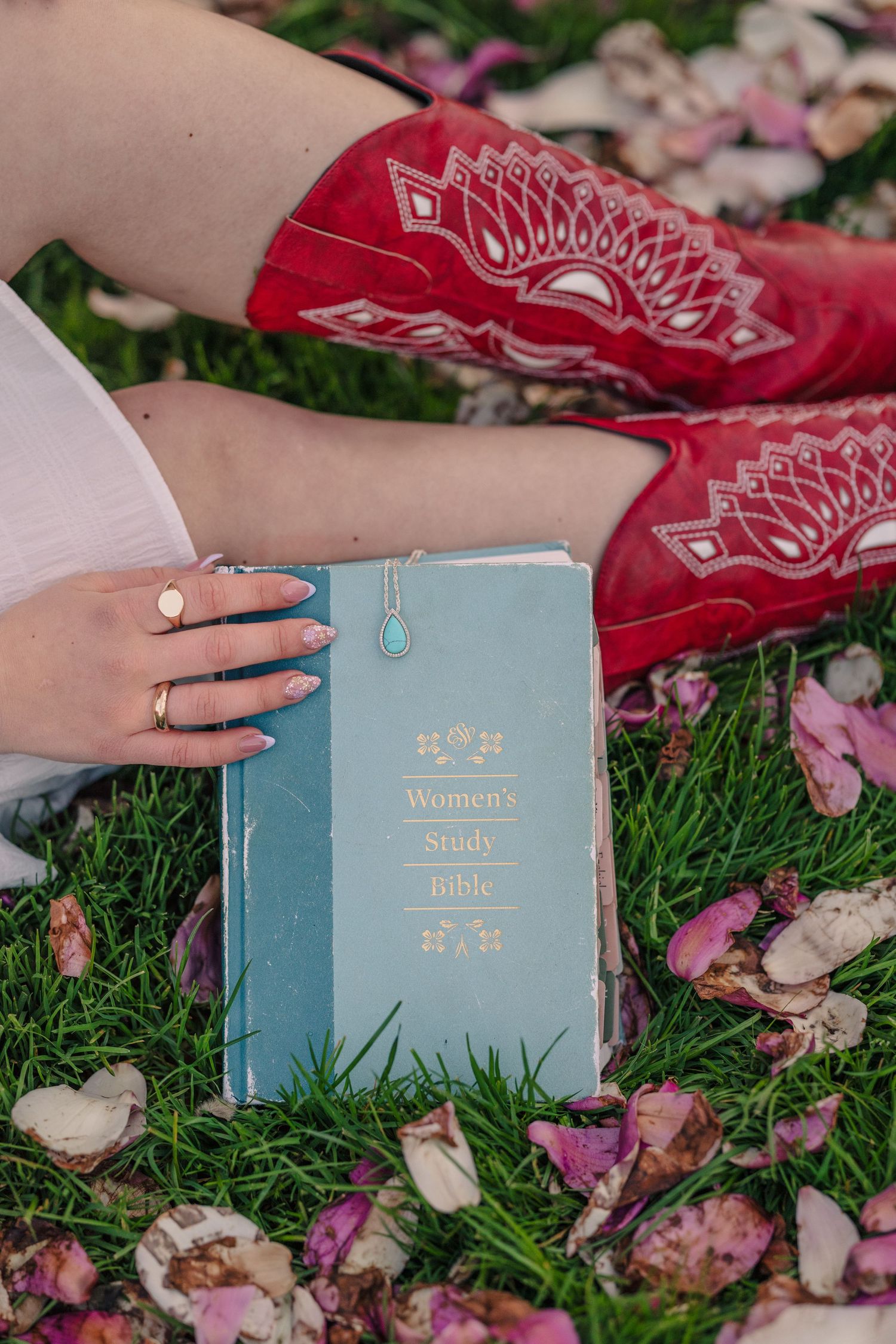 Light blue vintage books arranged on grass with scattered pink flower petals.