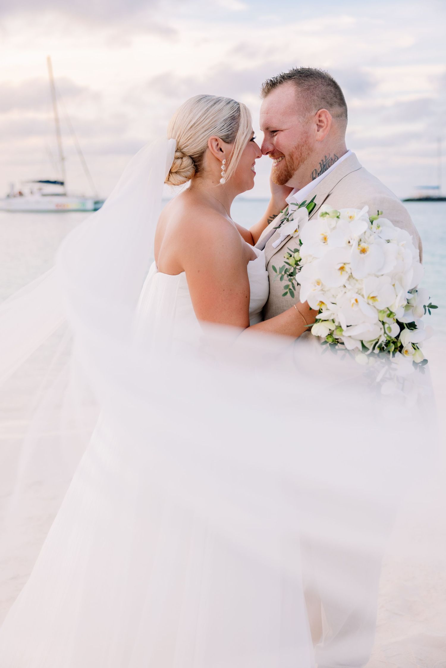 Romantic beach wedding portrait with white flowers and sailing boats in background.