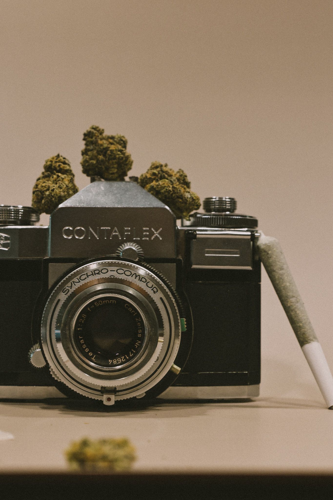 Vintage Contaflex camera with marijuana buds and a joint displayed artistically on neutral background.
