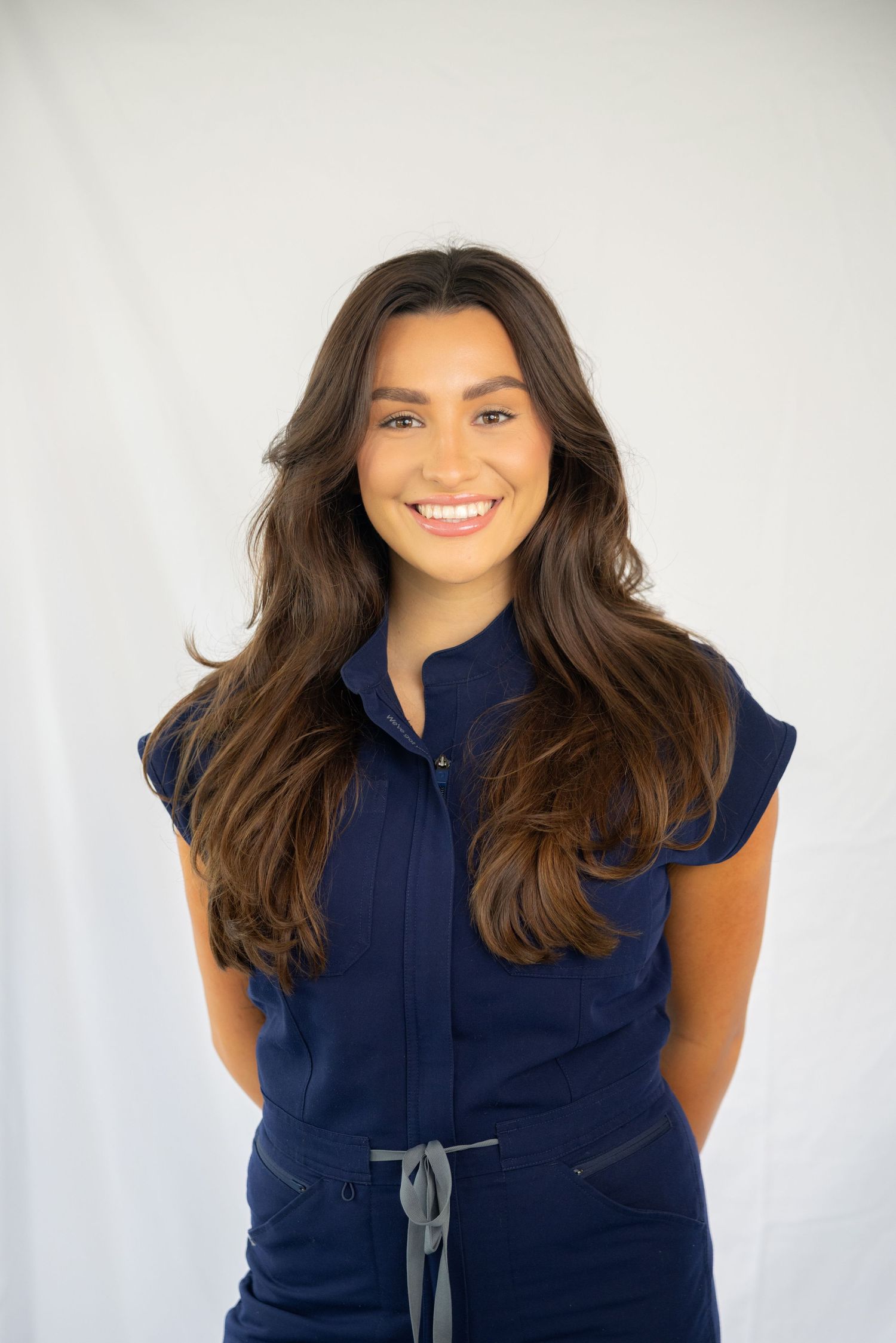 Professional portrait against white background wearing navy blue sleeveless top with casual styling.