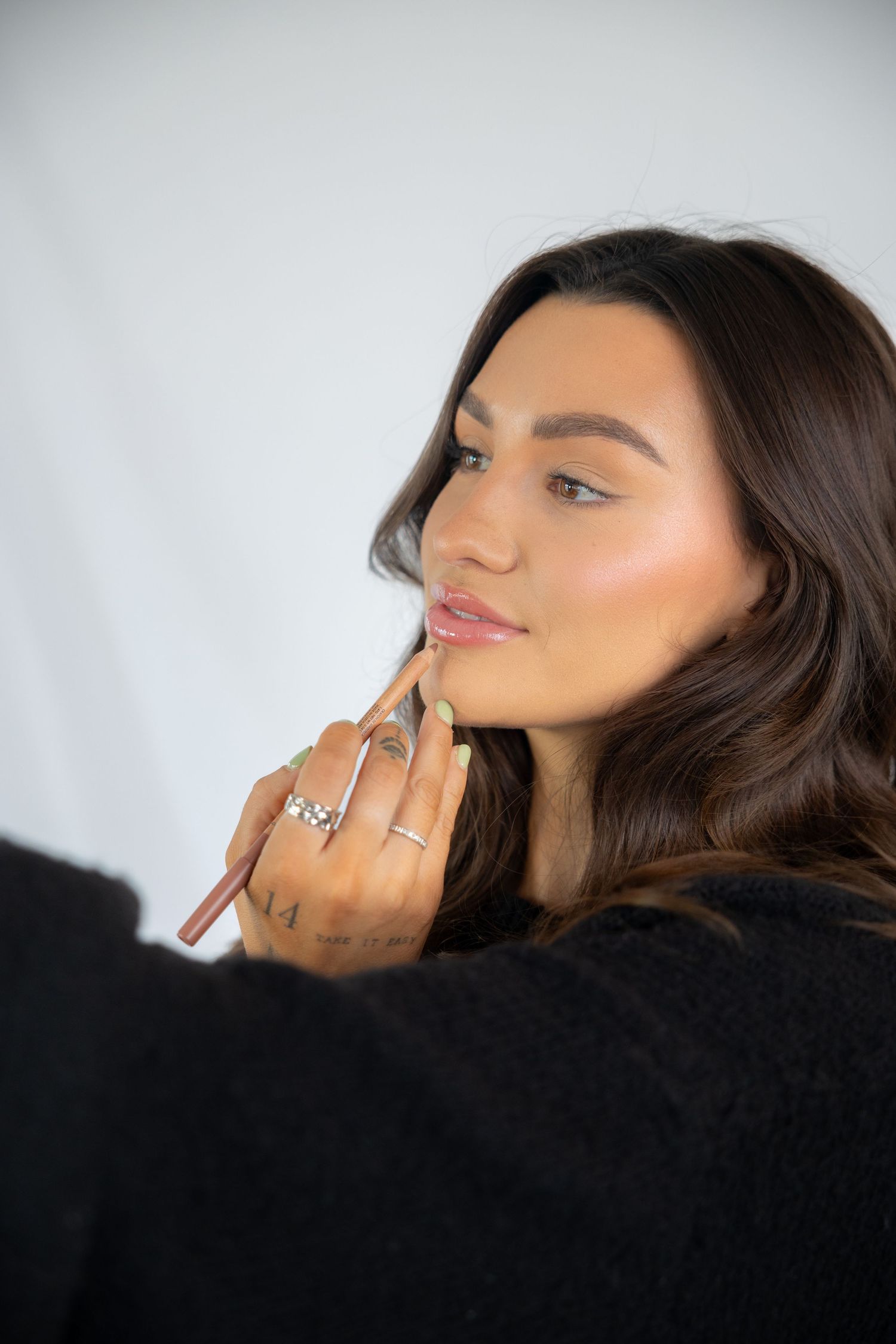 Close-up beauty shot showing hand with silver rings and pink lipstick against black sweater in dramatic lighting.