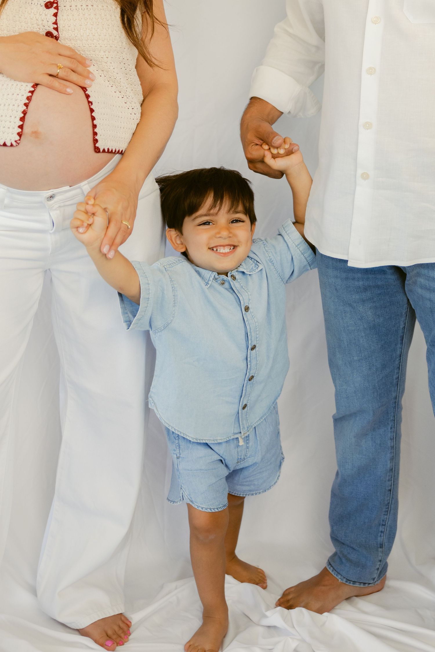 A small child in a light blue outfit holds hands with adults wearing white and denim in a series of candid photos.