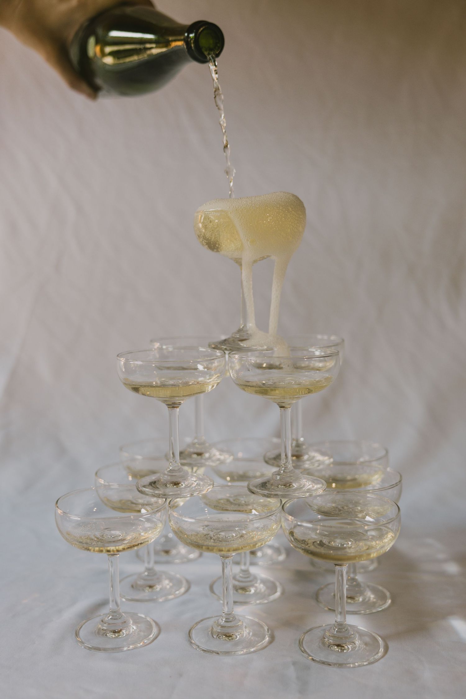 Champagne being poured into a set of vintage coupe glasses arranged in elegant pyramid formations.