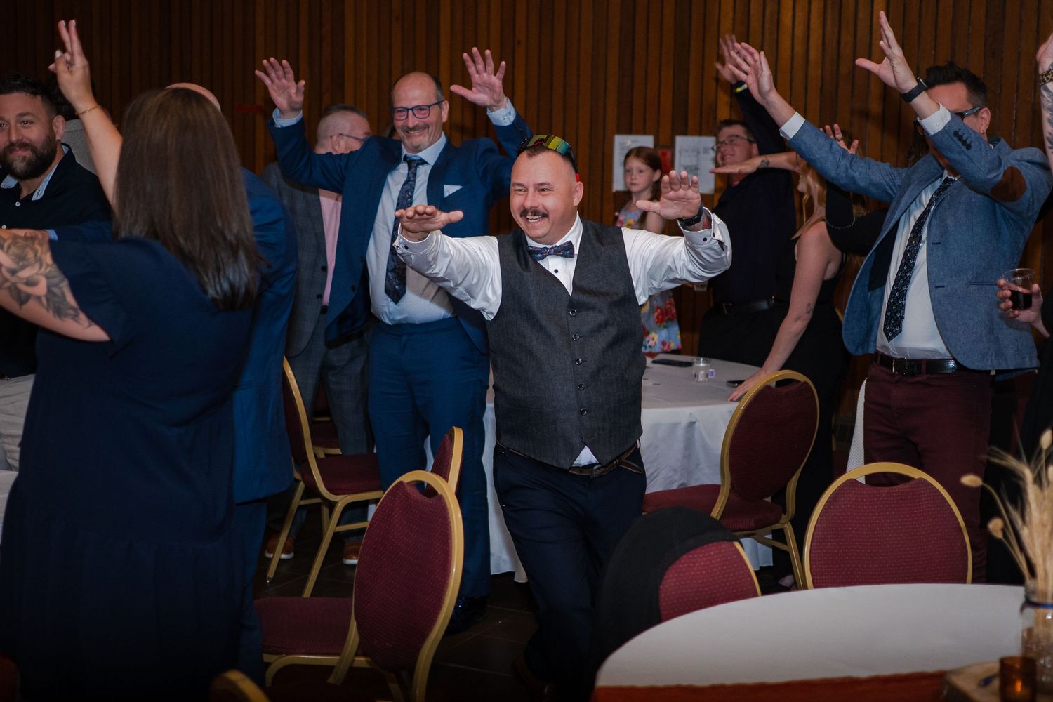 Wedding reception guests raising hands in celebration at indoor venue.