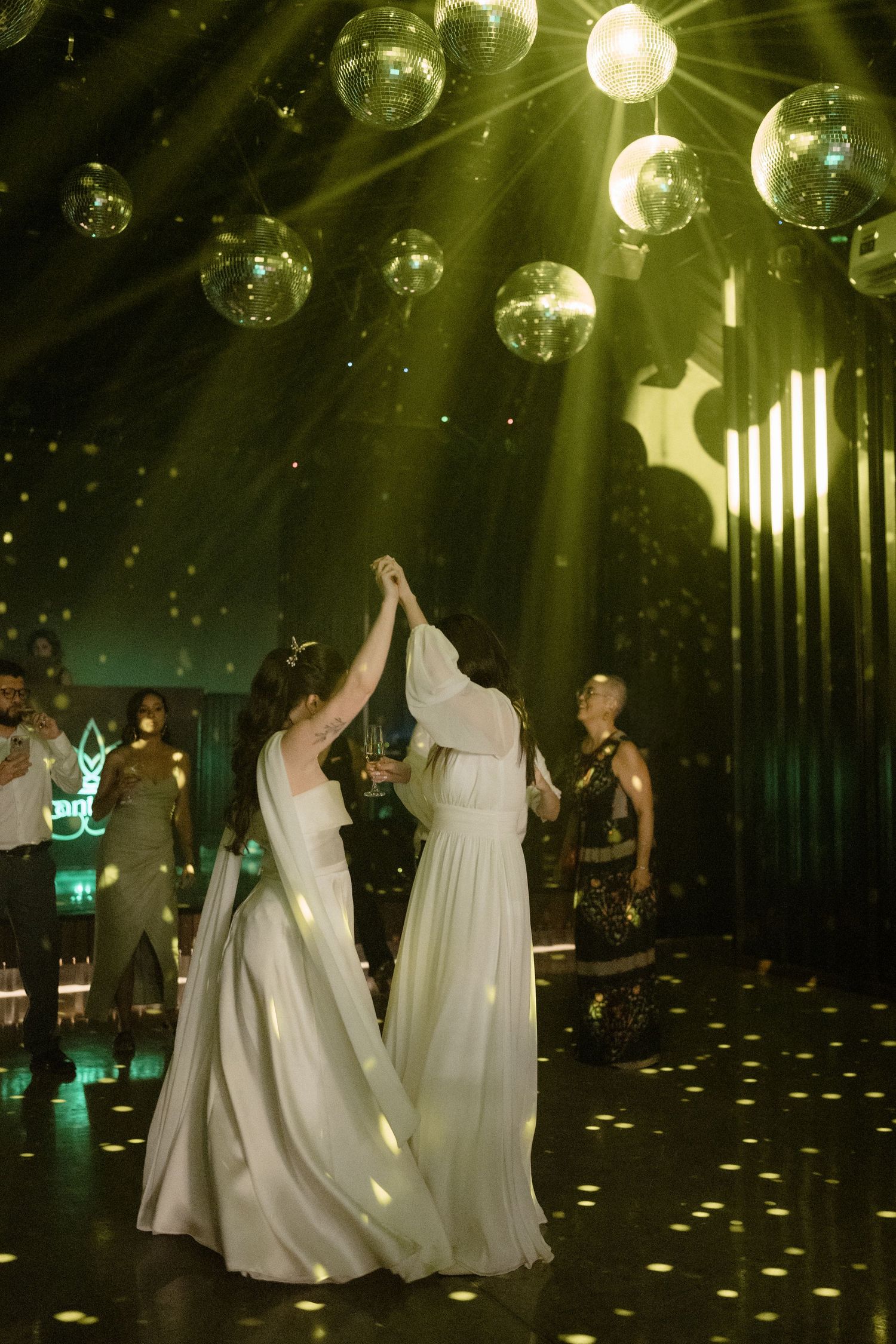 Wedding guests dance under glittering disco balls and spotlights on a dark dance floor with scattered light patterns.