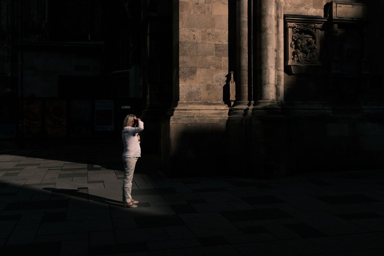 A person in white stands in a dramatic shaft of light against dark stone architecture.