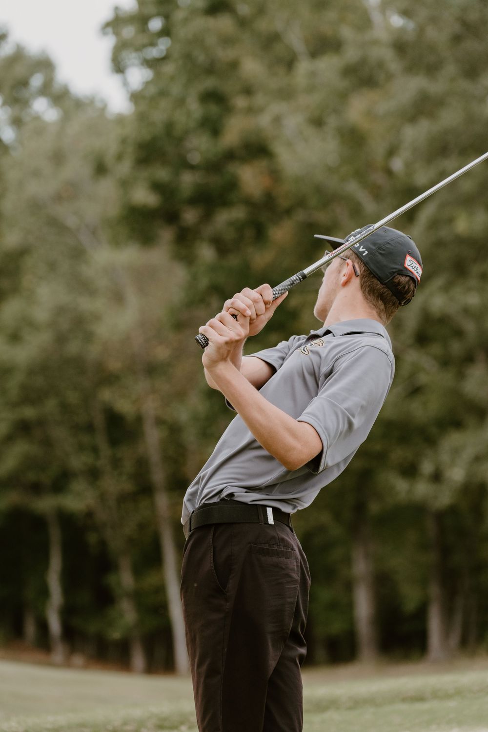 A golfer in grey attire demonstrates their swing form on a green course.
