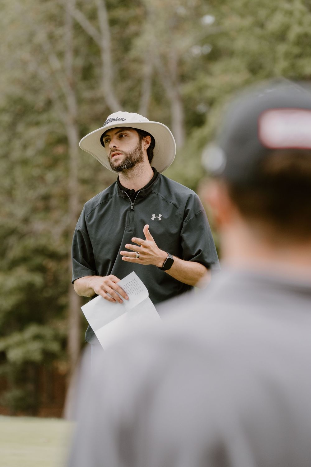 An instructor in athletic wear gives guidance to golfers on the course.