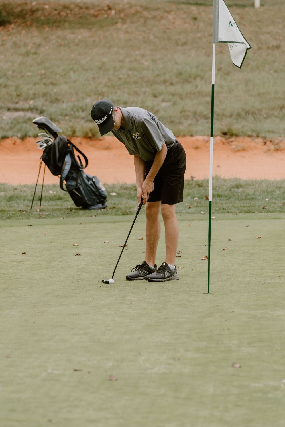 A golfer crouches down to analyze the putting green surface.