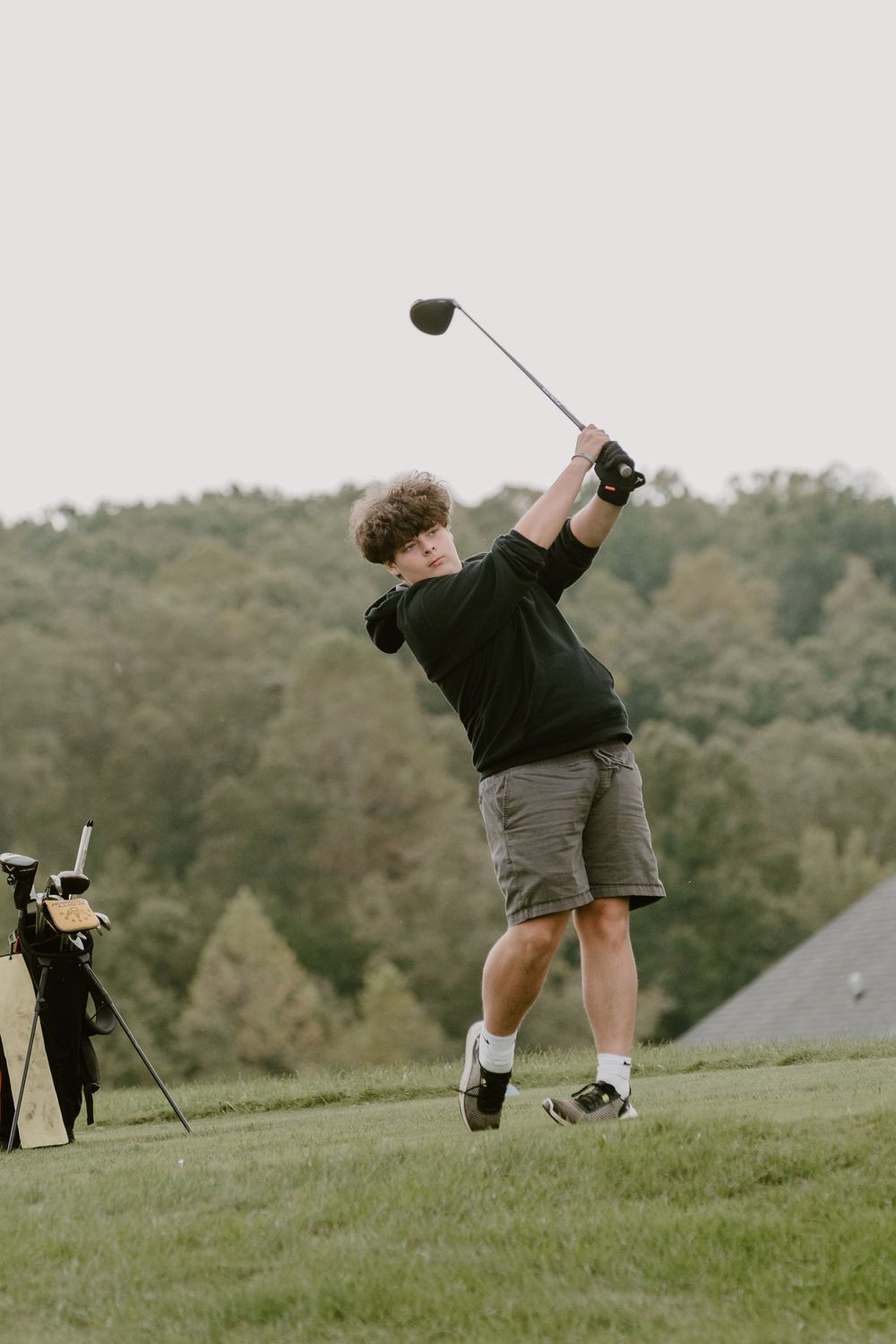 A golfer takes a powerful swing on a hilltop course with scenic views.