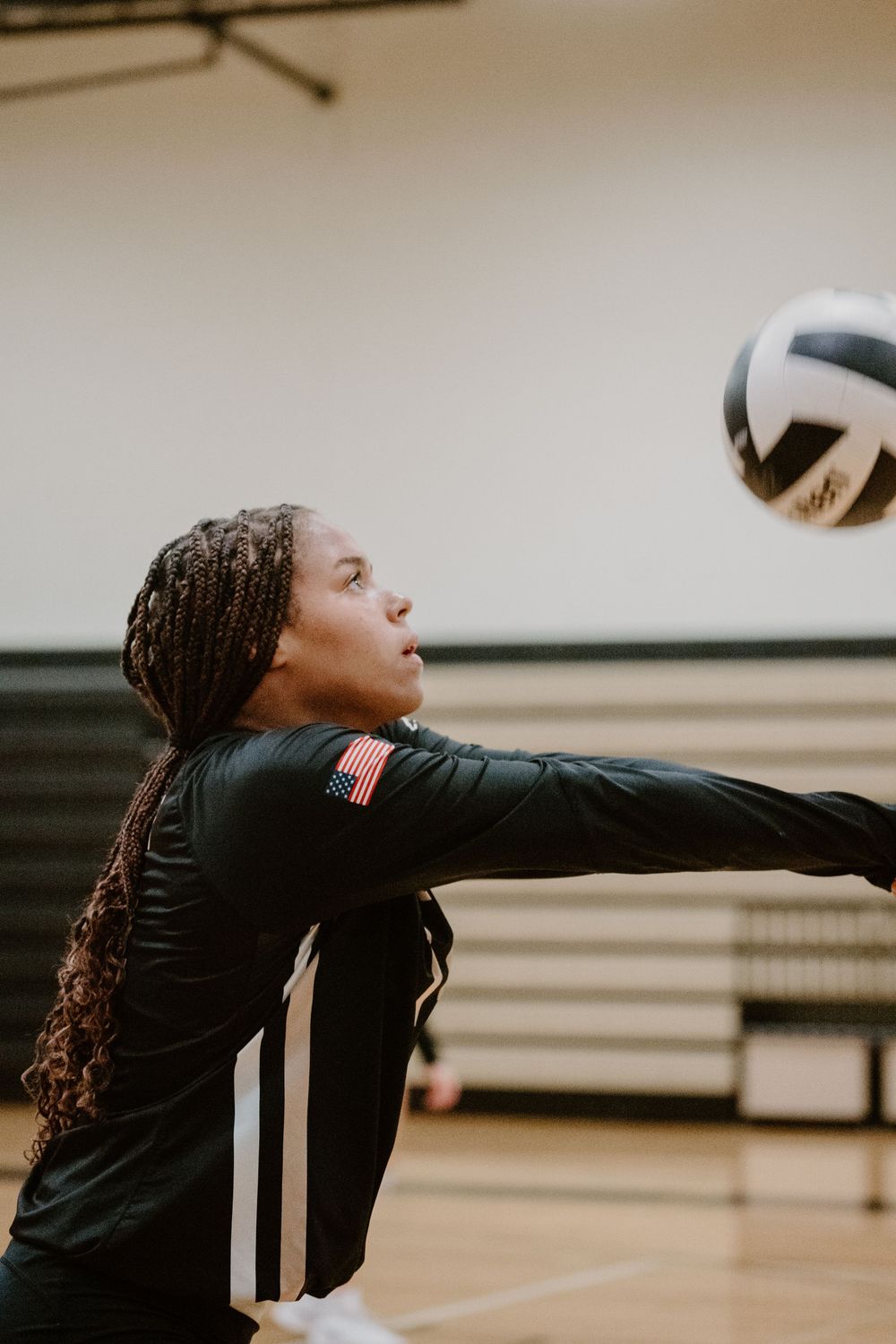 Volleyball player in black uniform with long braids prepares to hit the ball during an indoor match.