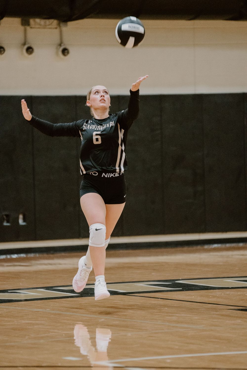 Volleyball player in black jersey serves the ball during an indoor match.