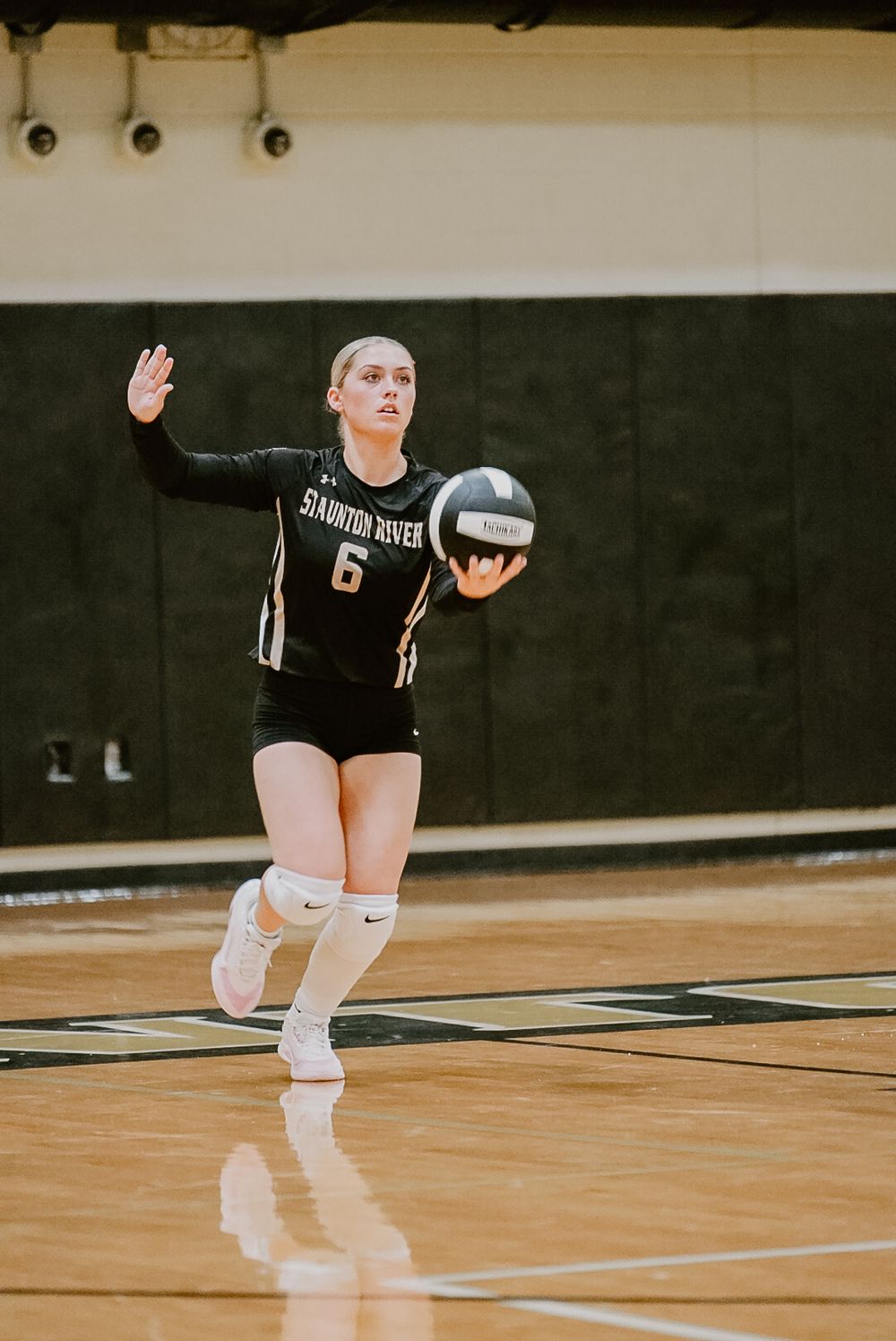 Player in black Staunton uniform prepares to serve during volleyball match.