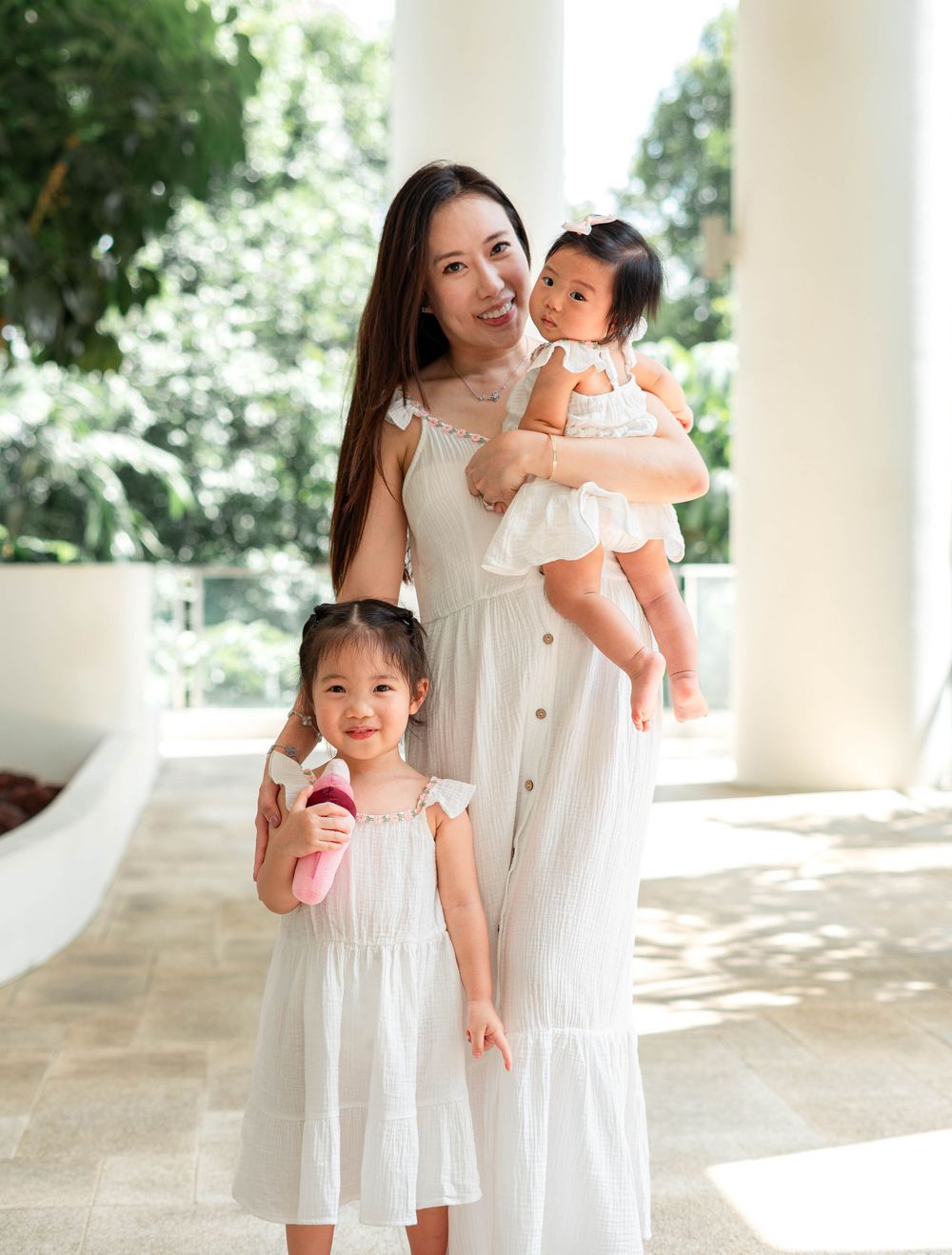 A family wearing matching white dresses poses together in a bright outdoor setting with white columns.