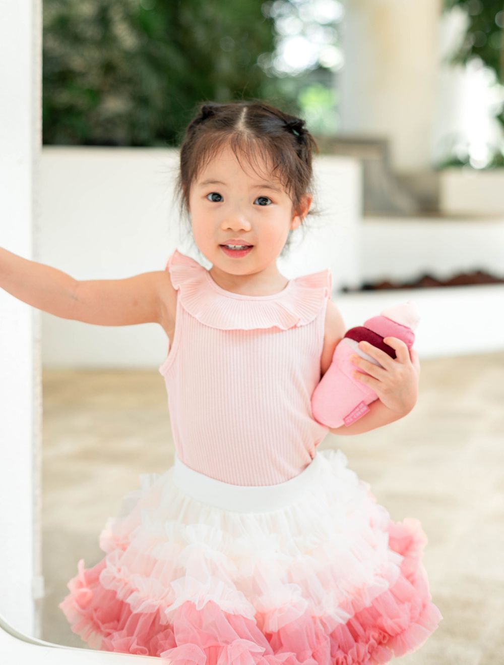 A child in a pink tutu dress with ruffles smiles and poses in three candid shots.