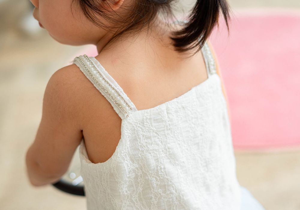 Child wearing a white sleeveless summer dress with lace straps against a pink background.