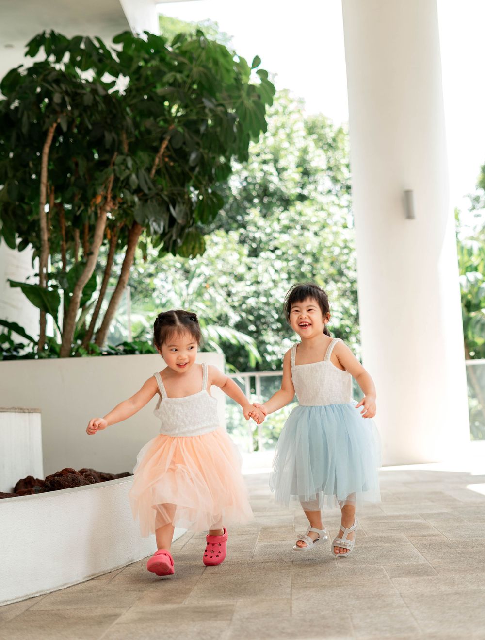 Two small children in tulle dresses dance and twirl together in a covered outdoor walkway.