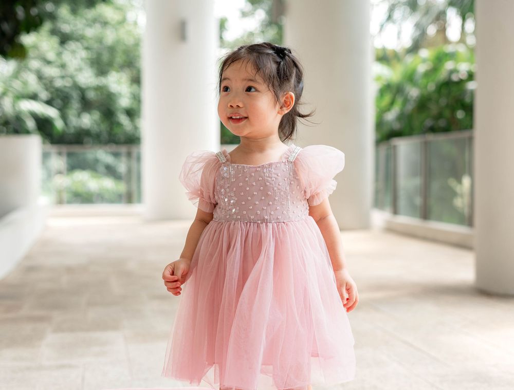 A small child in a pink tulle dress twirls and plays in a bright indoor space with natural lighting.