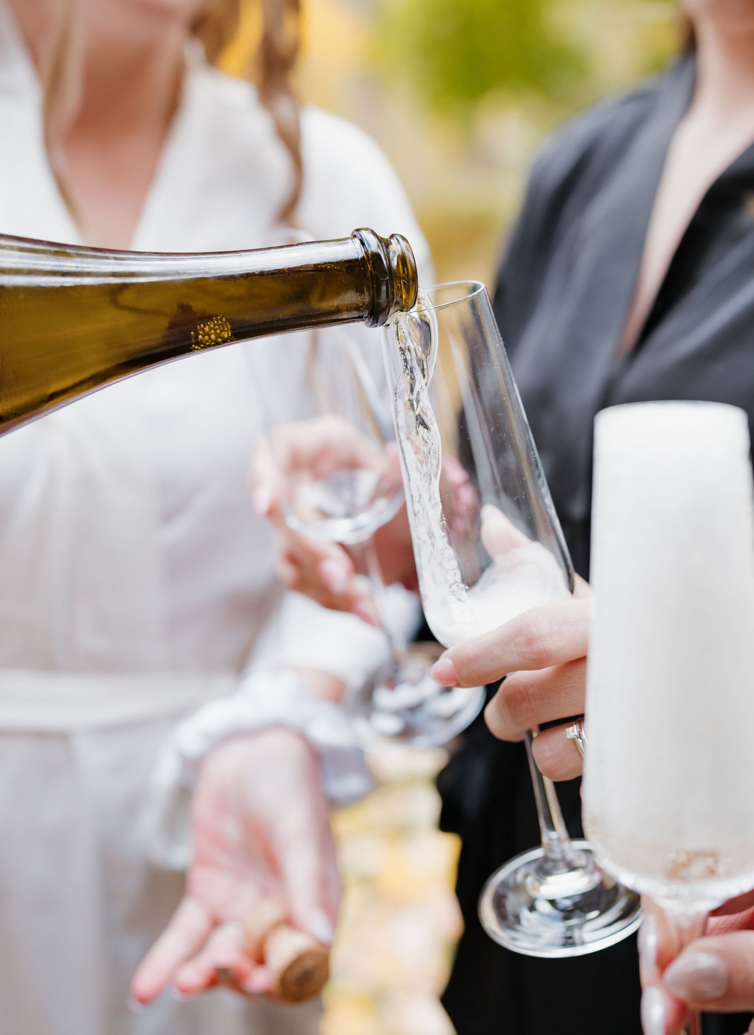 White wine being poured into an elegant glass at an outdoor gathering.