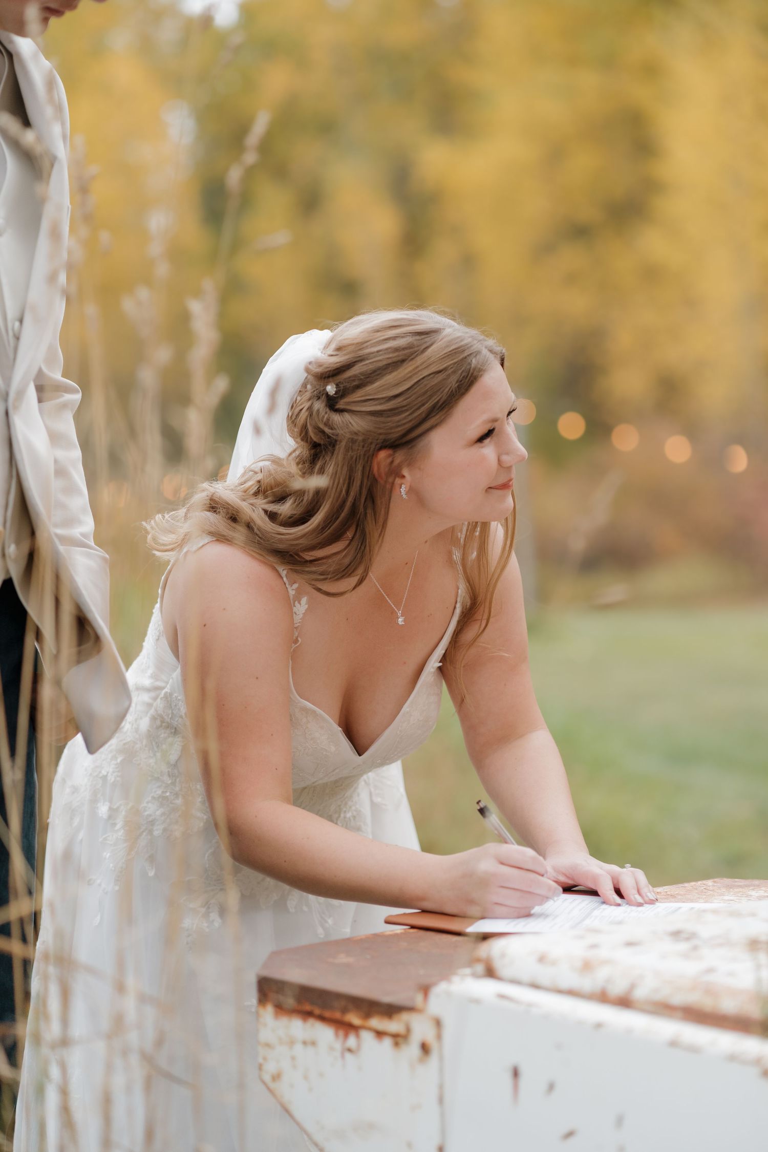 A bride in a white wedding dress leans over an antique table during an autumn outdoor photoshoot.