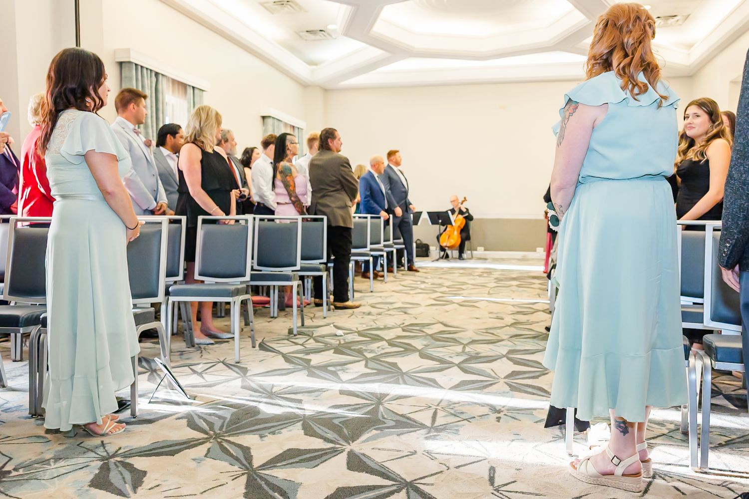 A row of people in blue and gray dresses stand in a carpeted conference room during a formal event.