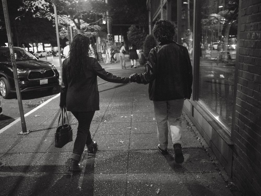 A queer couple holding hands while walking down the street in Seattle at night.