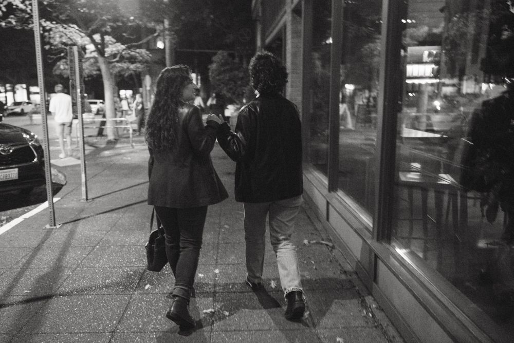 A queer couple holding hands while walking down the street in Seattle at night.