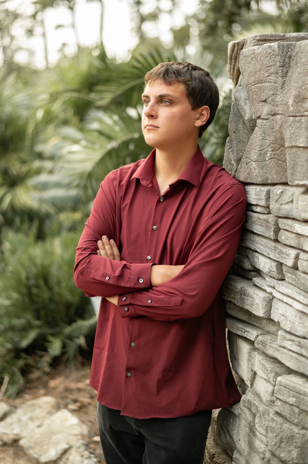 A series of portrait photos showing someone in a burgundy button-down shirt leaning against a stone wall outdoors.